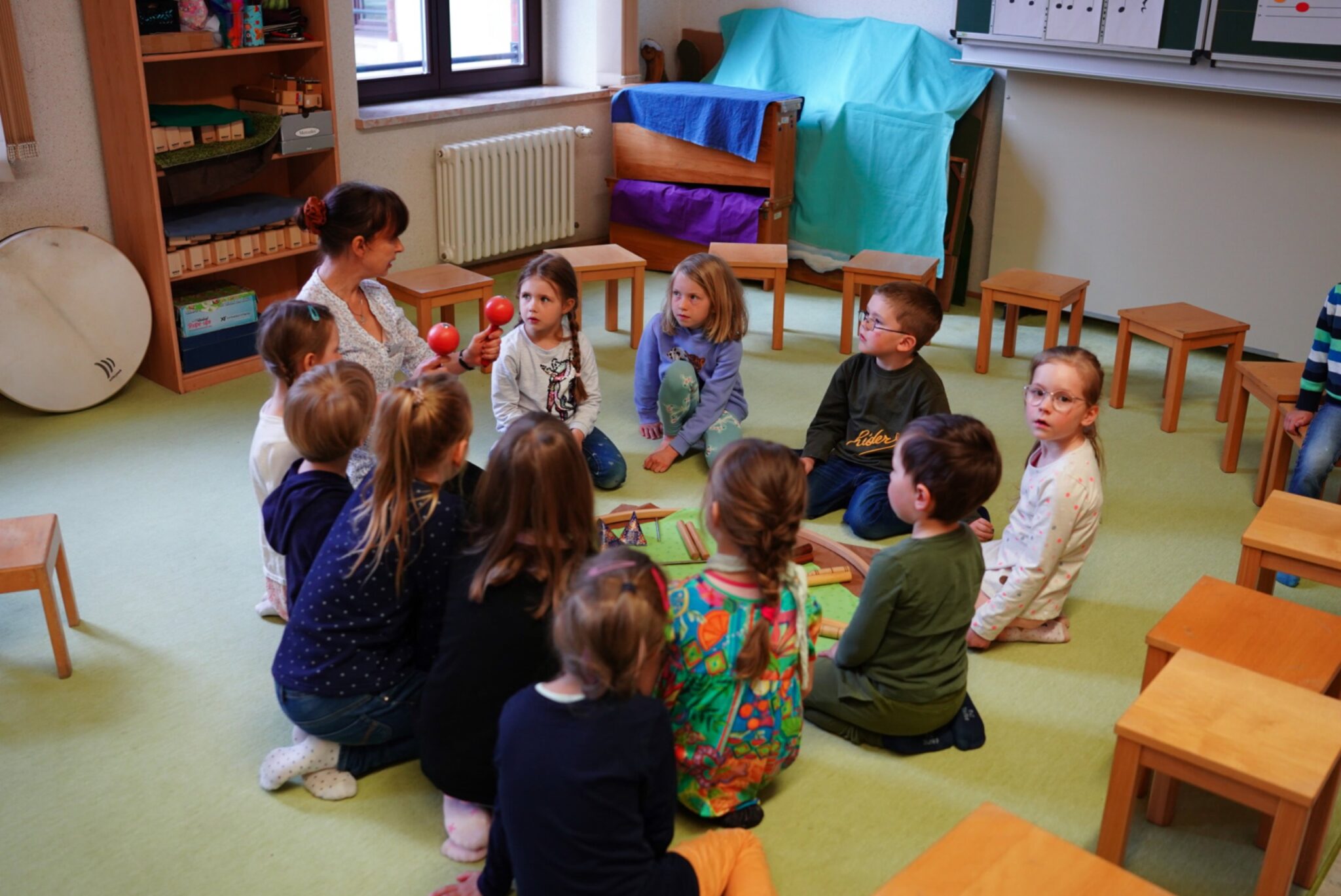 eine Gruppe Vorschulkinder sitz mit einer Lehrerin im Kreis und in der Mitte liegen verschieden Orff-Instrumente zur musikalischen Frühförderung
