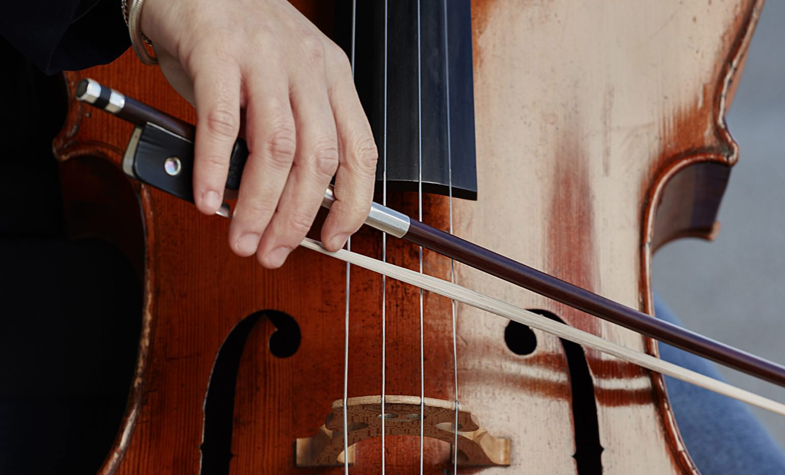 eine Hand mit einem Bogen streicht über die Seiten eines Cellos